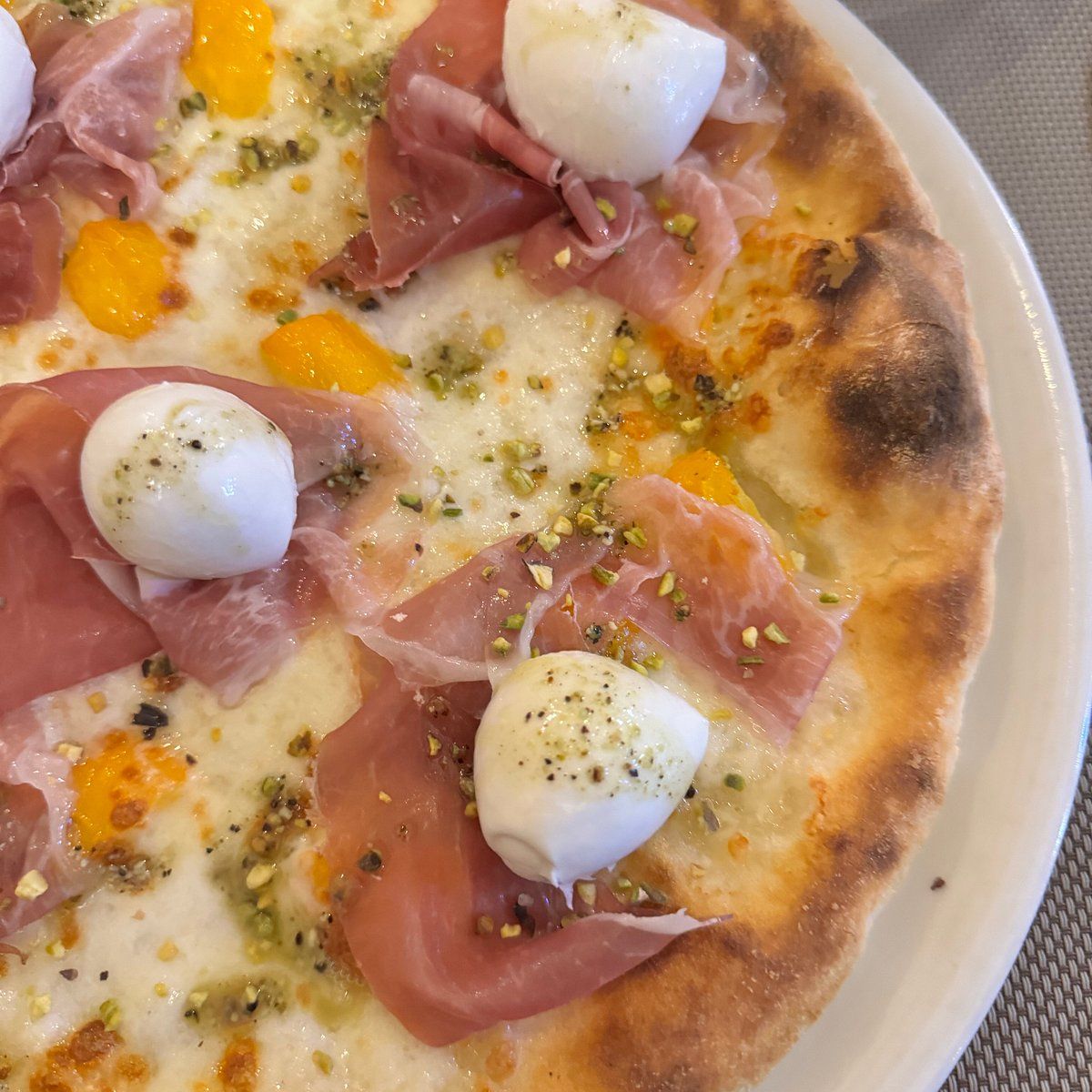Dettaglio di pizza artigianale con crudo, mozzarella e granella di pistacchio